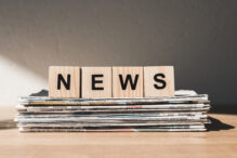 wooden blocks with news lettering on pile of print newspapers